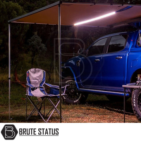 Camping setup featuring an ARB Simpson III Rooftop Tent & Annex on a blue off-road pickup, with awning, LED strip light, folding chair, and table visible under the awning.