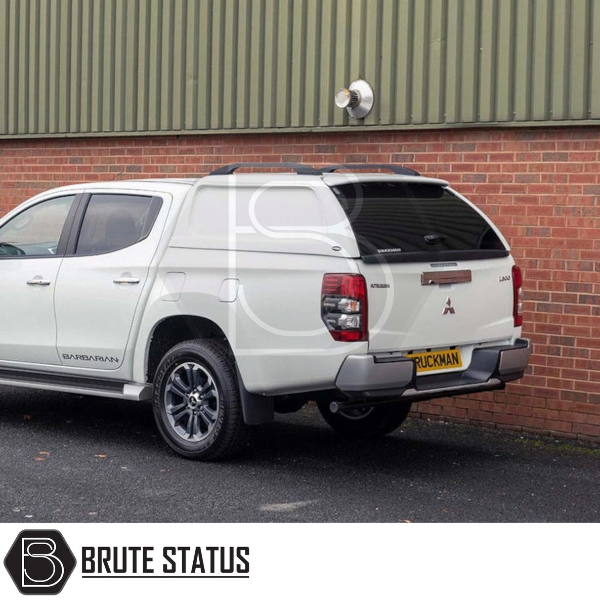 White Mitsubishi L200 with Truckman L-Series hardtop canopy featuring remote locking, parked by brick building, showcasing aftermarket accessory for enhanced security and style.