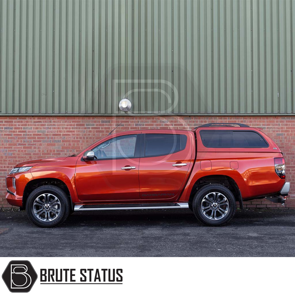 Metallic orange-red pickup with Truckman GLS hardtop canopy, featuring remote locking and sliding windows, parked in front of a brick and steel wall.