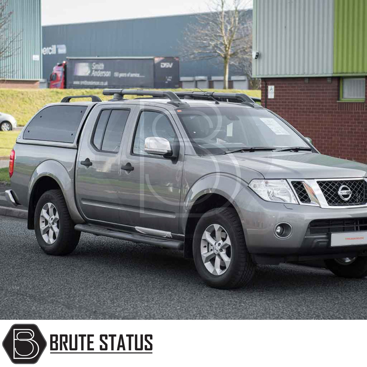 Silver-grey Nissan Navara with Truckman Grand Hardtop Canopy featuring remote locking, tinted pop-out windows, and a sleek cab-high design, parked in front of an industrial building.