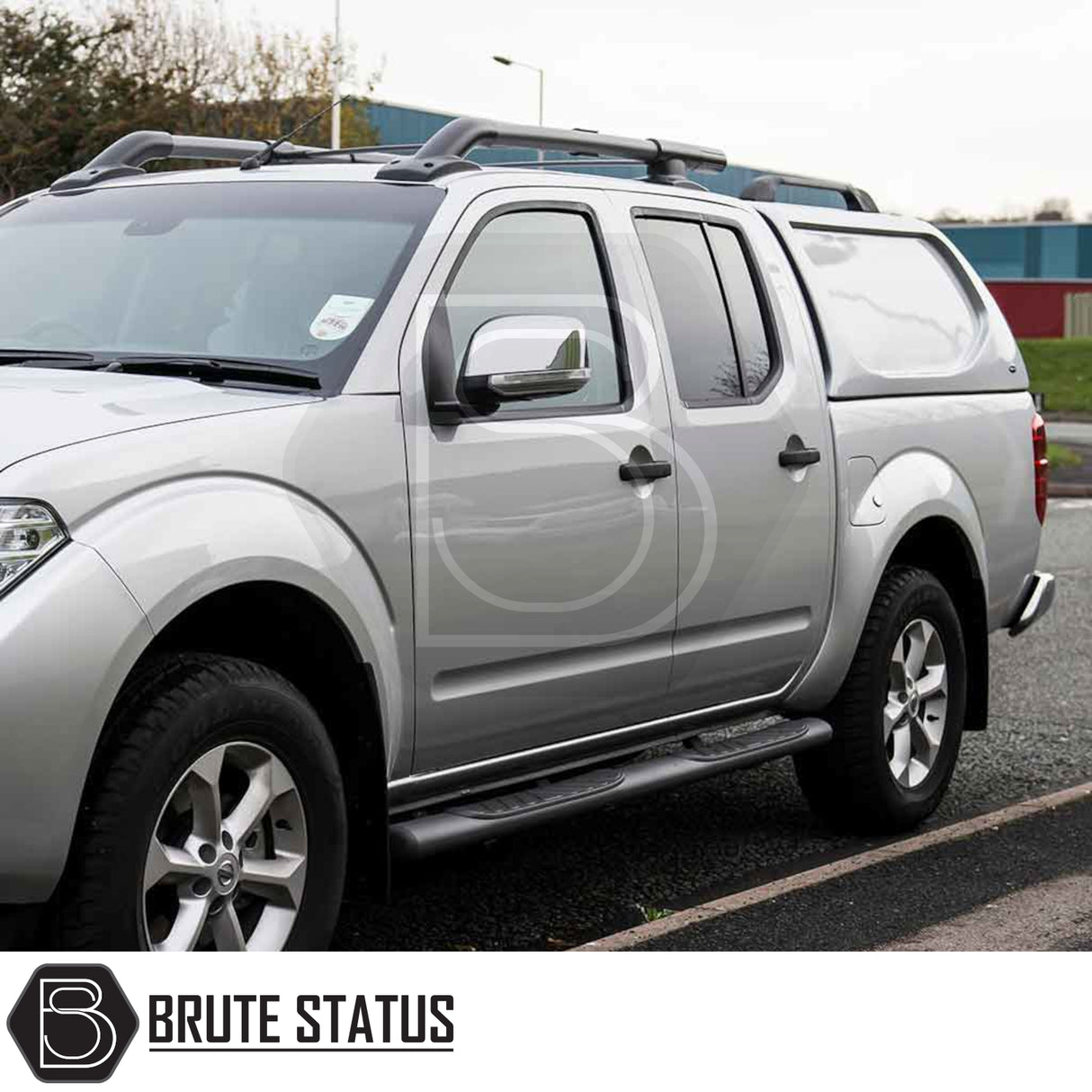 Silver Nissan Navara 2005-2015 D40 with Truckman L-Series Hardtop Canopy, featuring solid sides, roof rails, and side steps, in a promotional setting for Brute Status.