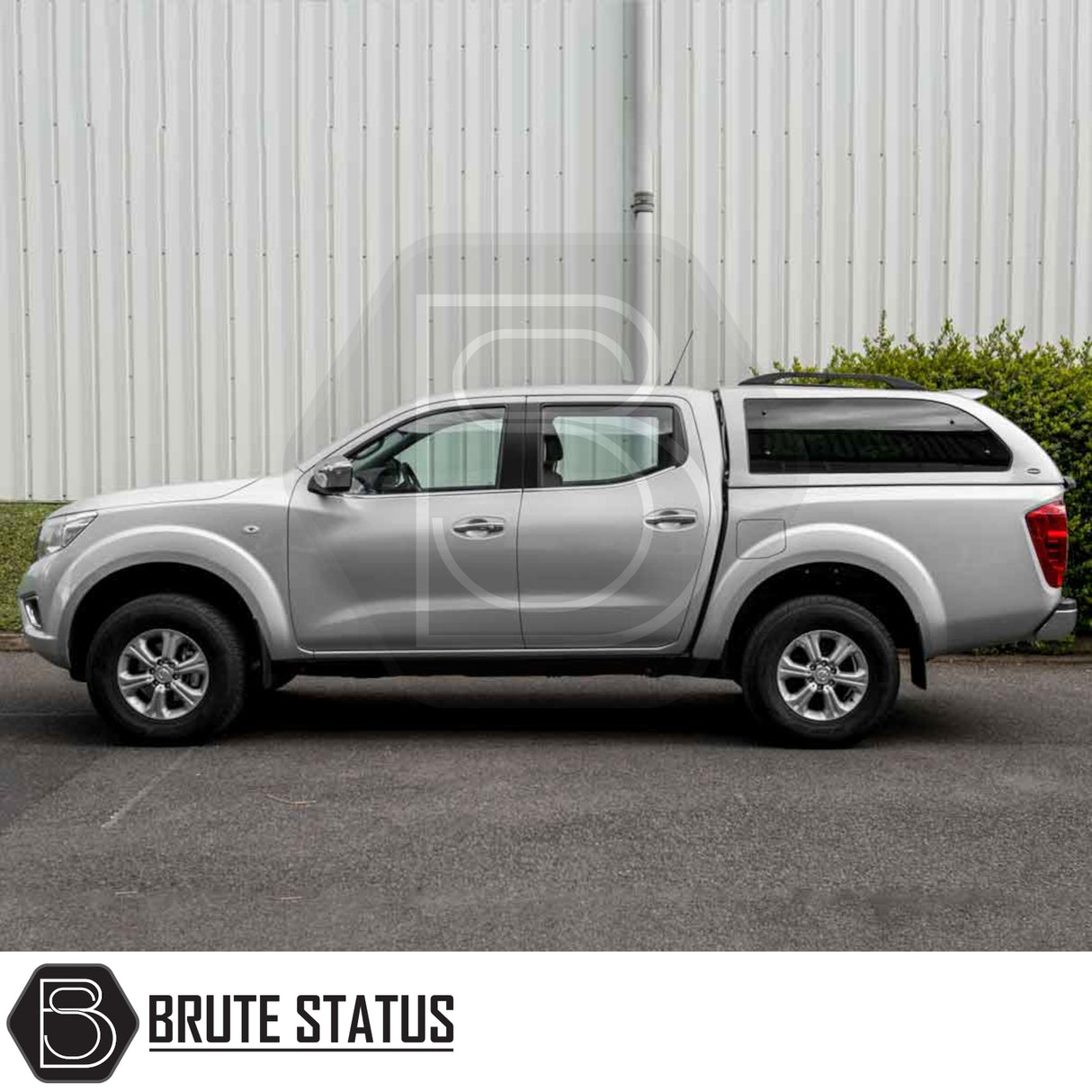 Silver Nissan Navara 2015-2023 NP300 with Truckman Grand Hardtop Canopy, featuring remote locking and tinted windows, parked in front of a corrugated-metal wall.