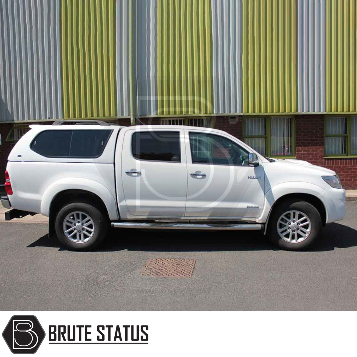 Toyota Hilux 2005-2016 MK6, MK7 with Truckman GLS Hardtop Canopy featuring remote locking, tinted sliding windows, and high-roof design, parked in front of a metal-sided building.