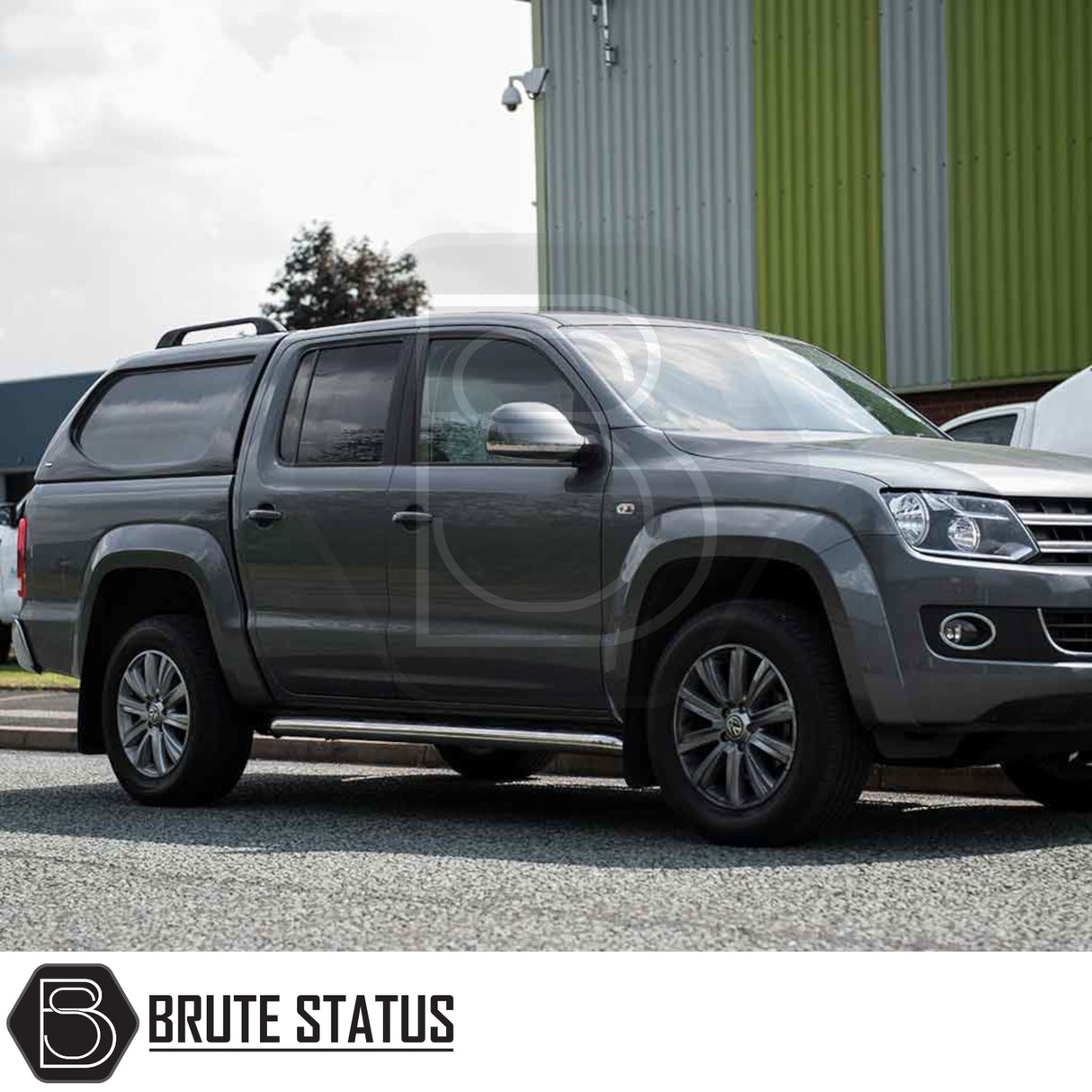 Grey VW Amarok with Truckman L-Series Hardtop Canopy, showcasing aftermarket design, chrome side-steps, alloy wheels, parked by industrial building.