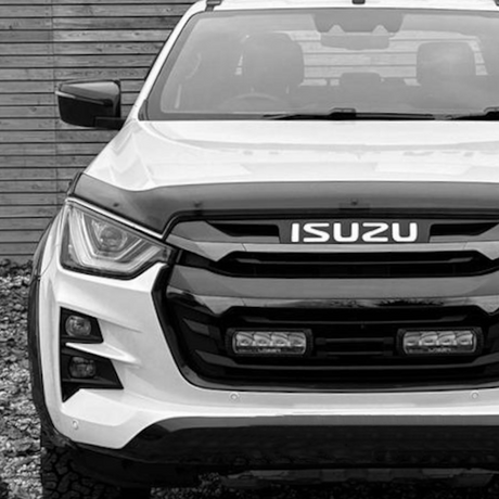 Front view of a white Isuzu D-ma parked in front of a wooden wall, showcasing its sleek design and aftermarket customizations.