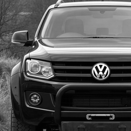 A black VW Amarok with a distinctive large emblem parked on a road, showcasing its sleek design and aftermarket enhancements.