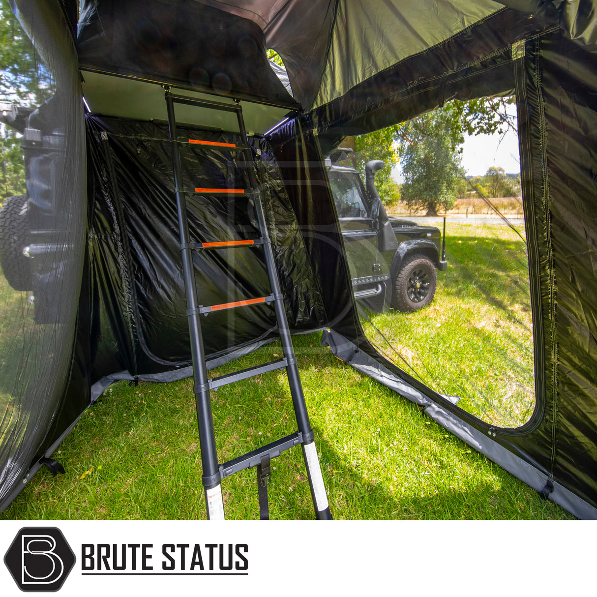Black SUV with ARB Esperance 2.0 Rooftop Tent Annex Room, featuring mesh windows and telescoping ladder, set at a grassy campsite, branded “Brute Status”.