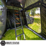 Black SUV with ARB Esperance 2.0 Rooftop Tent Annex Room, featuring mesh windows and telescoping ladder, set at a grassy campsite, branded “Brute Status”.