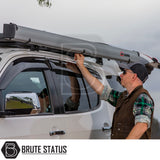 A man unfolds a silver ARB Awning Alcove from a white SUV's crossbars, showcasing its versatility for camping and overlanding enthusiasts.