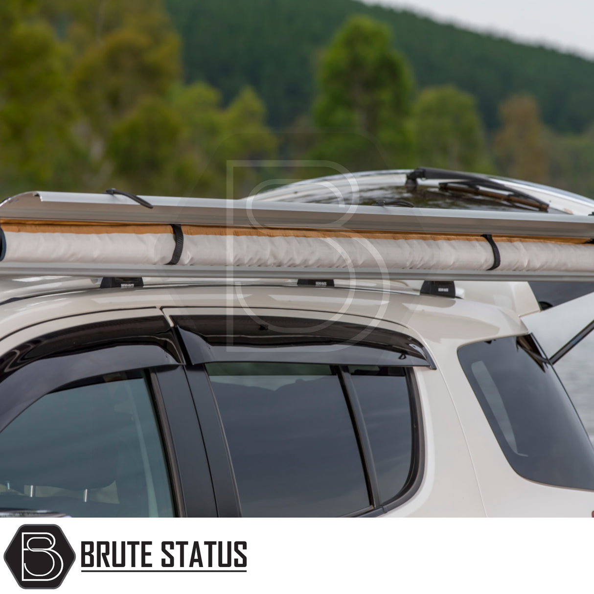 White SUV by lake with ARB Awning Alcove on roof bars, showcasing a rolled-up awning for versatile outdoor protection. Forested shoreline in the background.