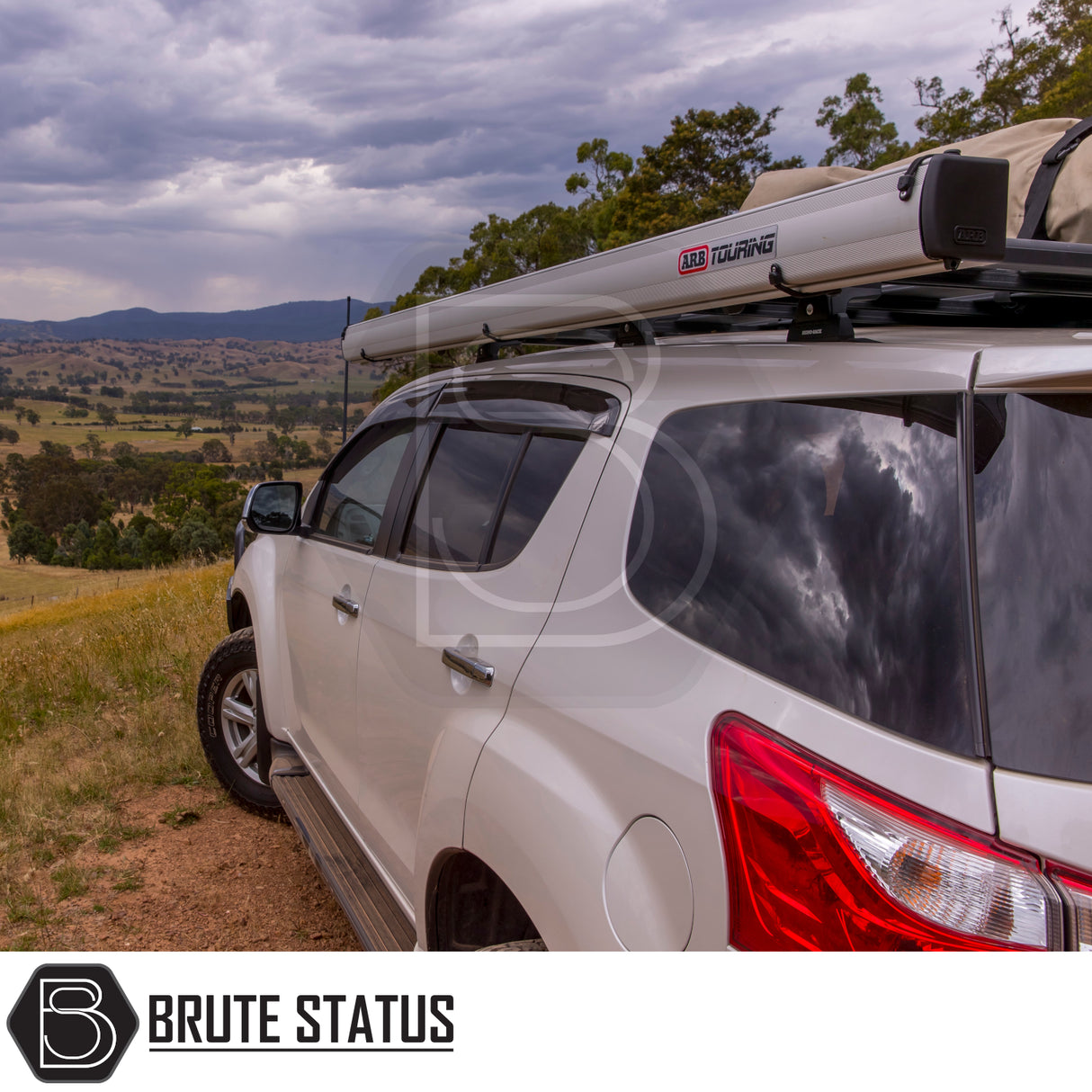 White SUV with ARB Aluminium Case Awning & LED Light Kit on roof, parked on grassy hill. Features chunky tires, side steps, tinted windows; ideal for off-road adventure.