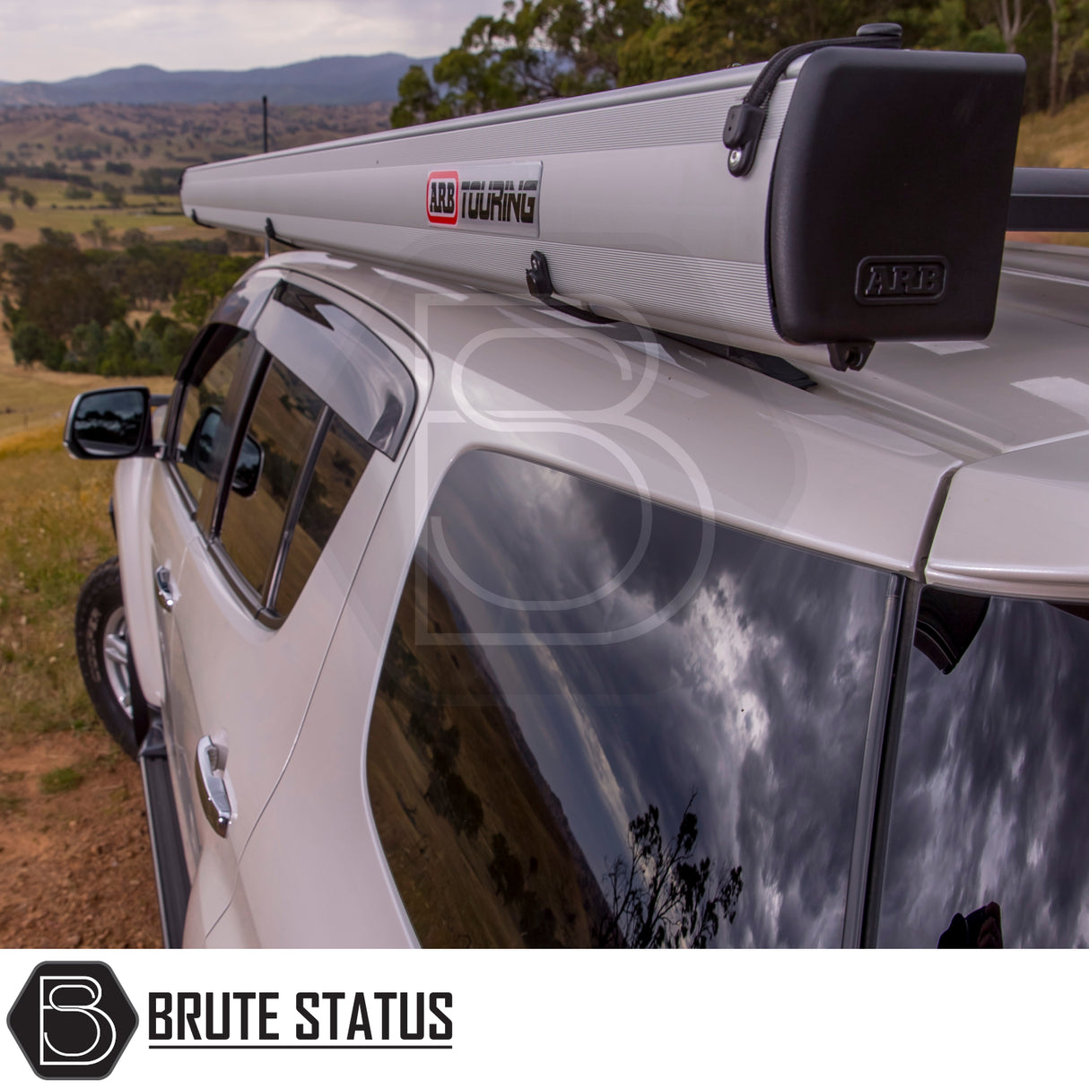 Silver off-road SUV with ARB Aluminium Case Awning on roof rack, in a grassy paddock, showcasing rugged durability and style for outdoor adventures.