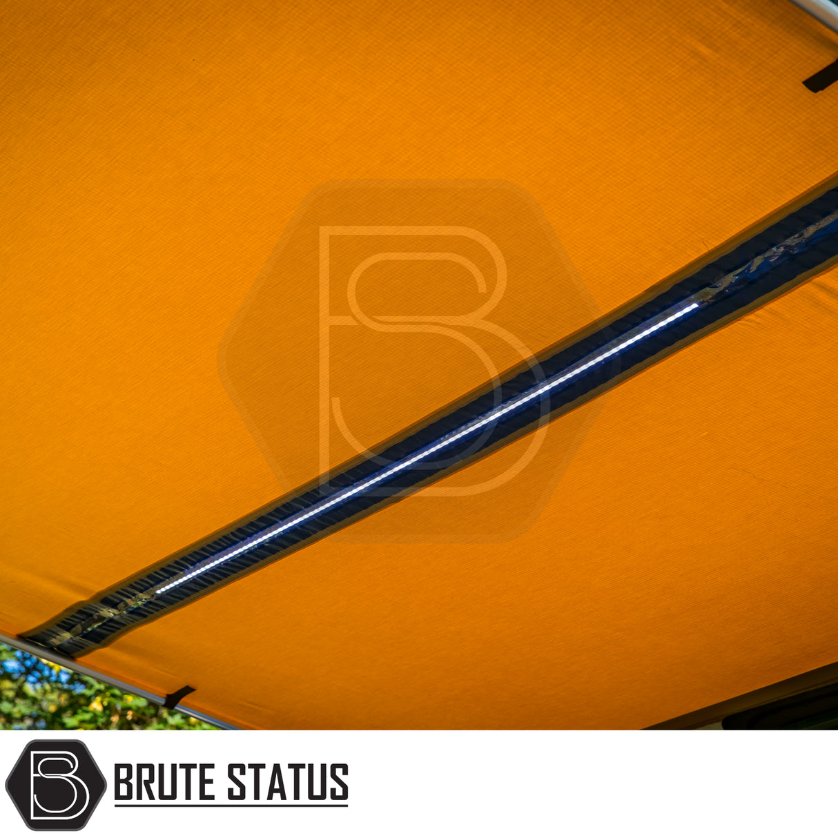 Outdoor retractable awning with orange fabric and central LED light, branded Brute Status, designed for versatile weather protection and storage solutions in camping environments.