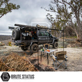 Off-road 4x4 setup with ARB Flinders Rooftop Tent, canopy, awning, gear shelves, and camping chairs, showcasing rugged self-sufficient camping on a rocky ledge.