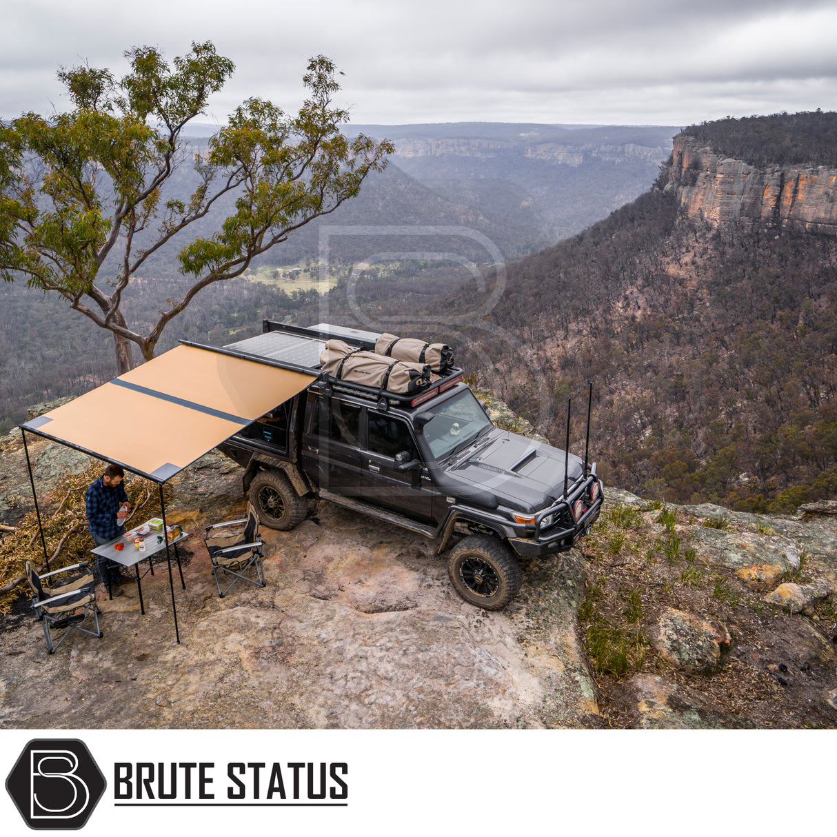 4x4 with ARB Aluminium Case Black Awning & LED Light Kit extended, set up with camping gear on a cliff, overlooking a forested gorge.