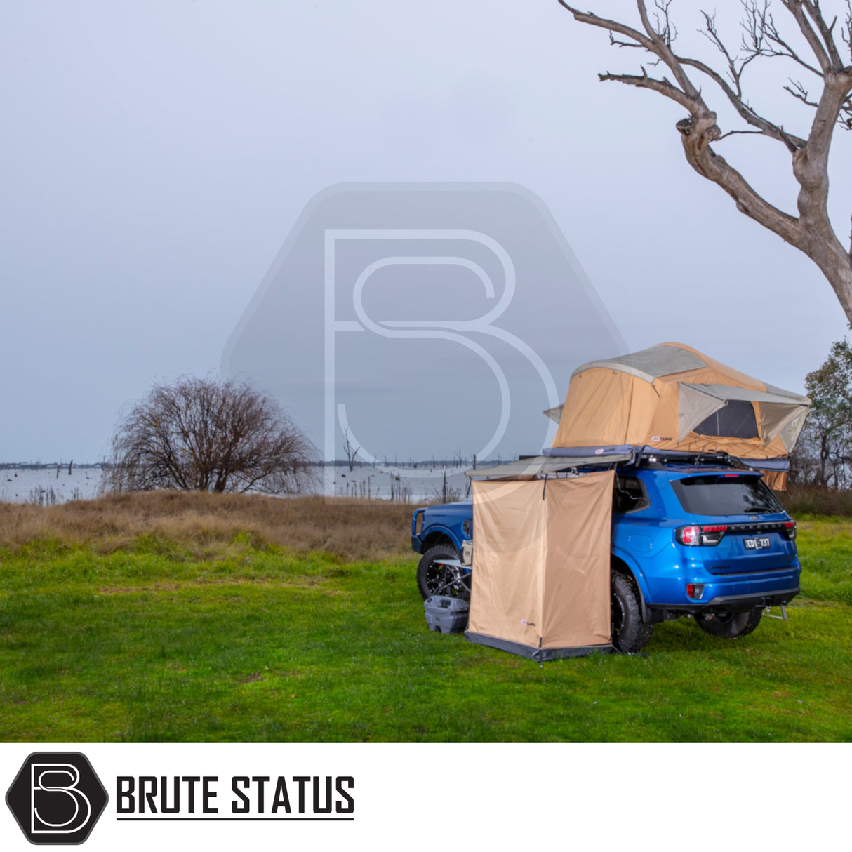Overland campsite with ARB Ensuite Room & Instant Shower Tent attached to a blue 4×4 SUV, featuring a roof-top tent and awning by a lakeshore.