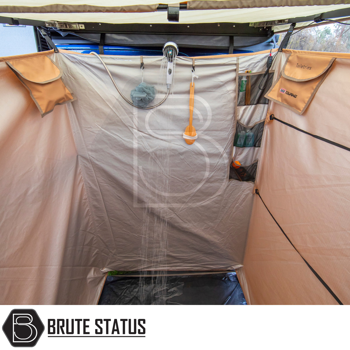 Inside view of the ARB Ensuite Room & Instant Shower Tent with mounted shower head, toiletries storage, waterproof floor, and Brute Status logo.