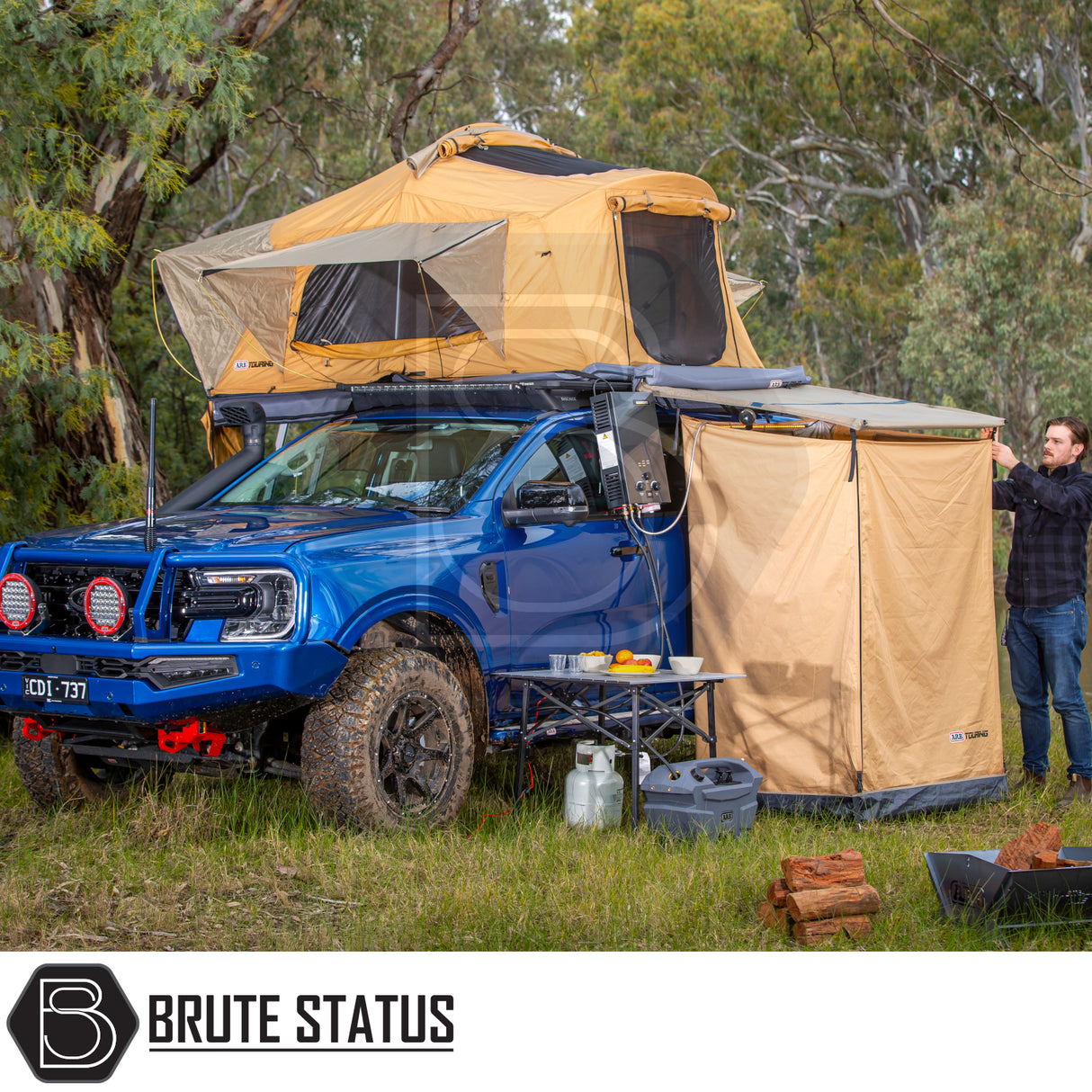 Blue 4x4 ute with ARB Flinders Rooftop Tent setup, featuring a pop-up tent, fold-out annex, camping essentials, and BRUTE STATUS branding visible.