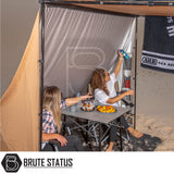 Two women enjoy a beach campsite under a Brute Status-branded ARB Awning Alcove, showcasing its versatile protection and organized storage features.