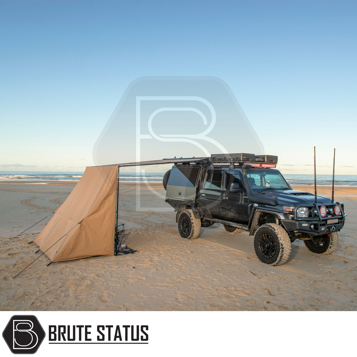 Black utility vehicle with ARB Aluminium Case Black Awning & LED Light Kit extended on sandy beach, showcasing off-road camping setup with roof rack and side awning.