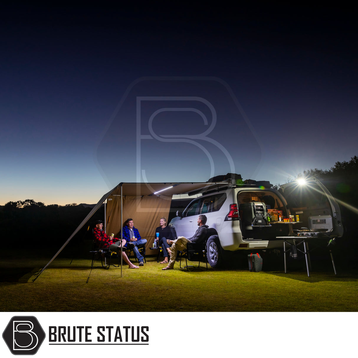 White SUV with ARB PVC Case Awning & LED Light Kit extended; people seated under awning, camp kitchen illuminated by LED lights, set in a grassy twilight clearing.