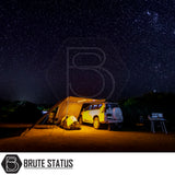 Nighttime camping scene with a white SUV featuring an ARB PVC Case Awning & LED Light Kit, illuminated campsite setup under a starry sky.