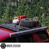 Red off-road SUV with ARB Awning 2m x 2.5m stored on roof rack, alongside spare tire, jerry can, propane cylinder, high-lift jack, and recovery boards.