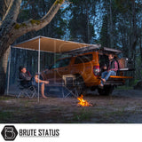 Two men enjoy a campsite beside an orange 4×4 truck with an extended ARB Awning 2m x 2.5m, featuring a rooftop awning and gear drawer.