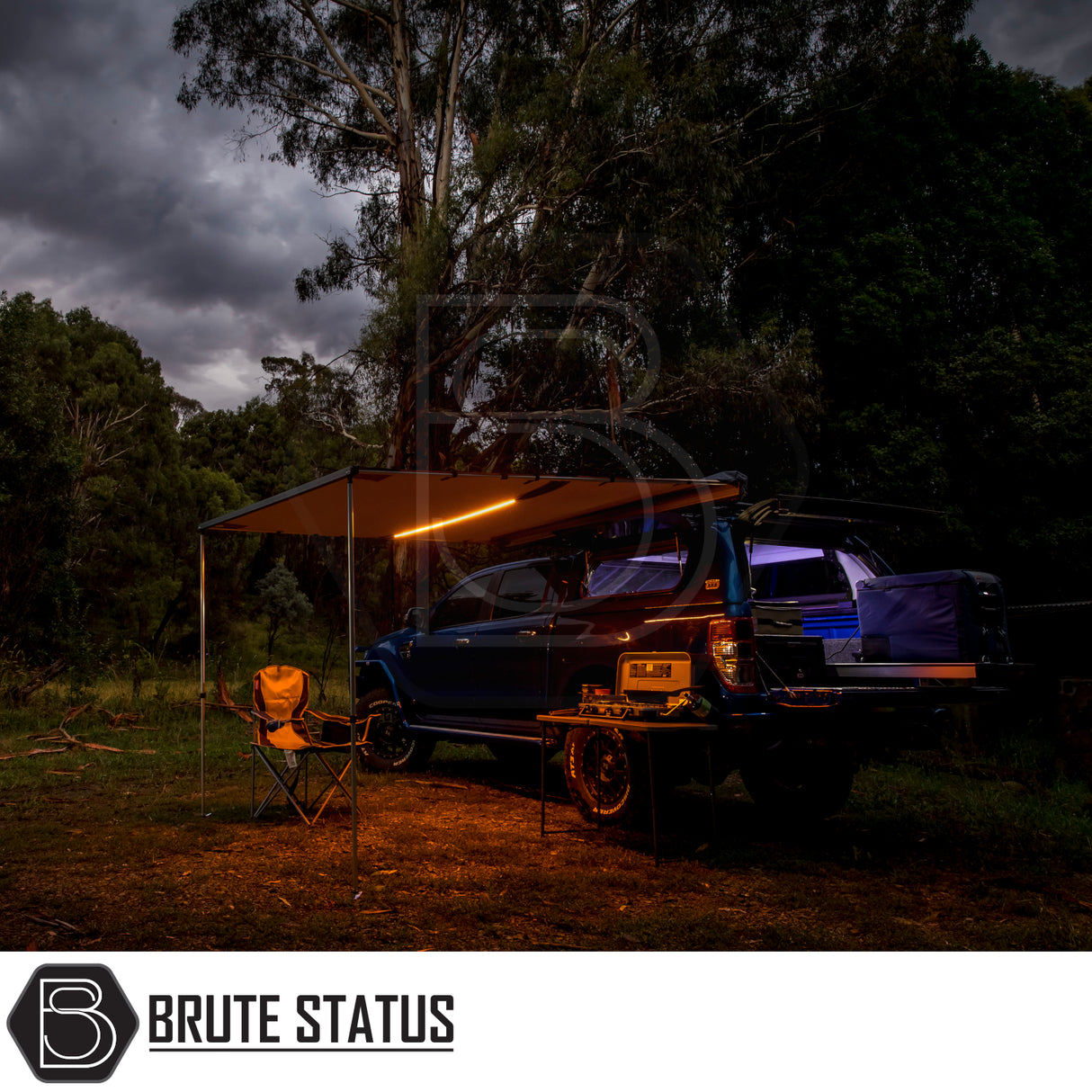 Blue 4x4 ute with ARB Awning Alcove, featuring LED-lit pull-out awning, camp chair, and slide-out kitchenette under gum trees at dusk.