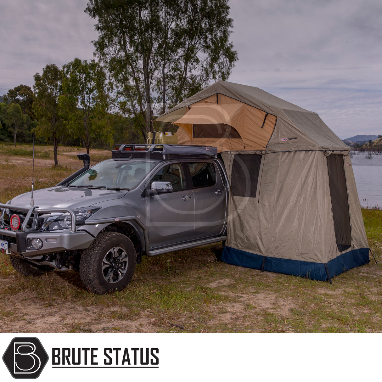 Silver 4×4 with ARB Simpson III Rooftop Tent and Annex, parked lakeside, showcasing overland camping setup with jerry cans, bull-bar, and winch.