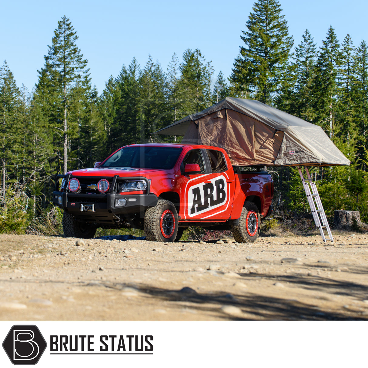 ARB Simpson III Rooftop Tent on a red pickup in a forest clearing, showcasing its fold-out design and aluminum ladder for enhanced camping convenience.