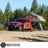 ARB Simpson III Rooftop Tent on a red pickup in a forest clearing, showcasing its fold-out design and aluminum ladder for enhanced camping convenience.
