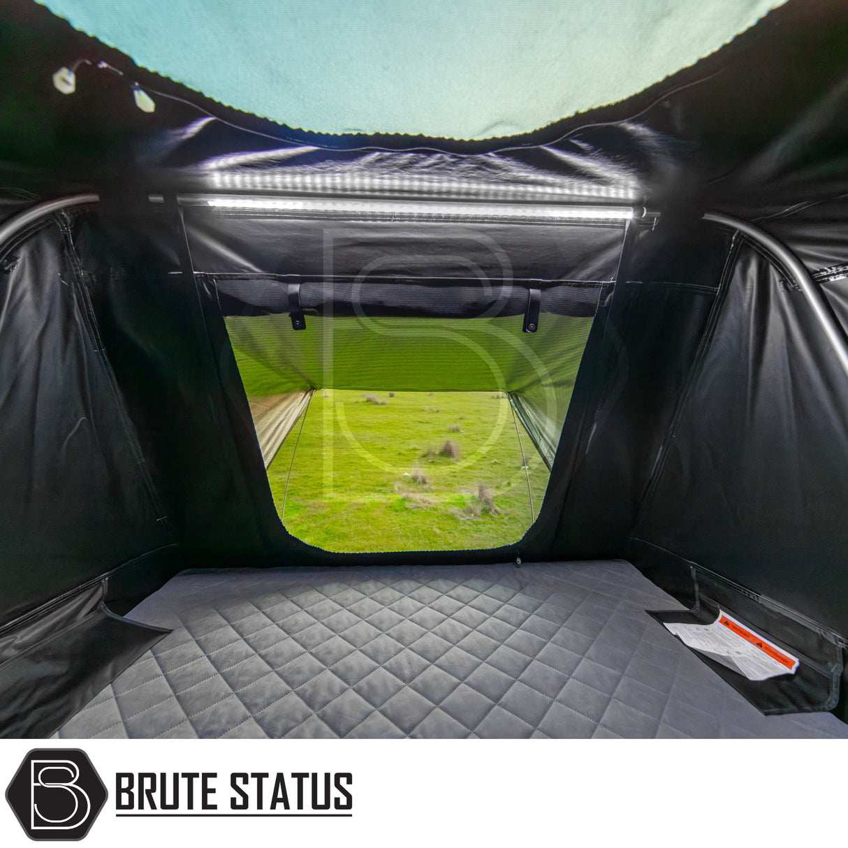 Interior view of ARB Esperance 2.0 Rooftop Tent featuring a quilted mattress, LED light strip, and zip-open window overlooking a grassy field.