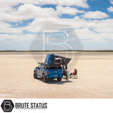 Bright-blue Ford pickup on salt flat with ARB Esperance 2.0 Rooftop Tent unfolded; red-shirted person seated nearby, capturing an adventurous camping setup.