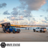 Seaside scene with 4x4 trucks; left truck features an ARB Esperance 2.0 Rooftop Tent, showcasing camping setup with anglers in the distance.