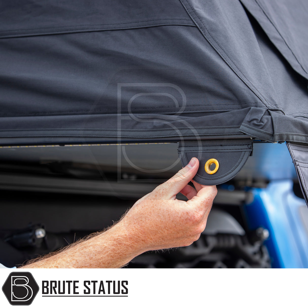 Hand pulling black canvas tab with brass grommet on ARB Esperance 2.0 Rooftop Tent Hard Shell, showcasing vehicle-mounted accessory by Brute Status.
