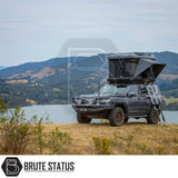 Toyota Land Cruiser-style SUV with ARB Altitude Rooftop Tent, featuring a pop-up design and ladder, parked on a grassy bluff overlooking scenic lake and hills.