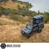 Heavily-modified 4×4 with ARB Altitude Rooftop Tent atop a grassy hillside, featuring a bull-bar, dual antennas, and a lockable canopy for overlanding.