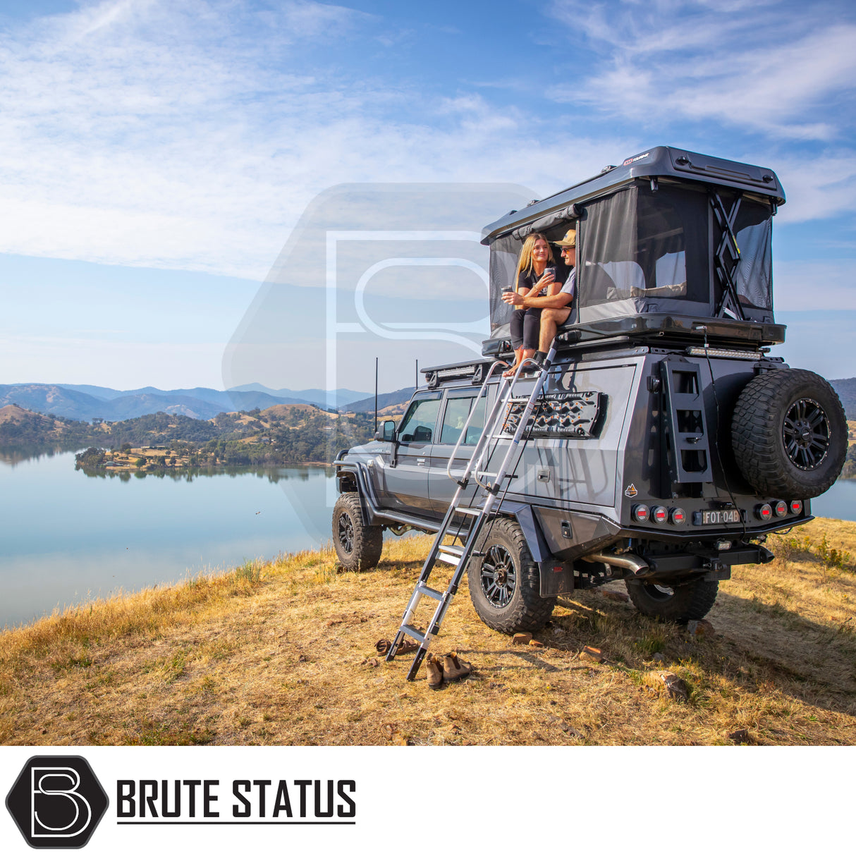 ARB Altitude Rooftop Tent set up on a Brute Status off-road camper truck, overlooking a lake and hills, showcasing luxury outdoor living.