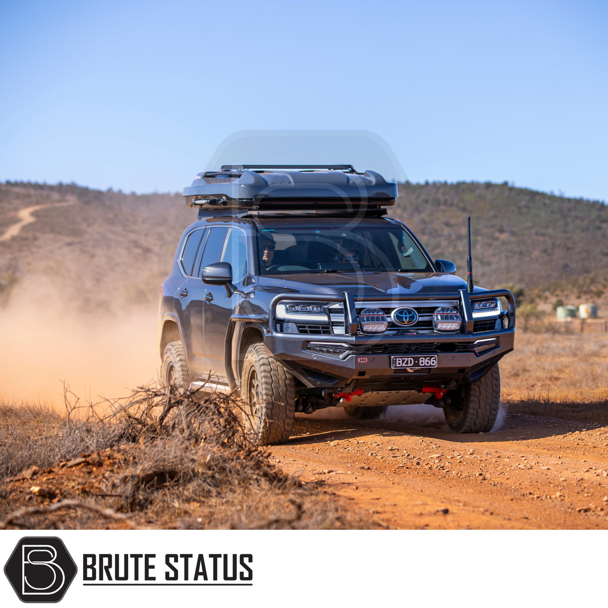 Toyota Land Cruiser with ARB Altitude Rooftop Tent on dirt track, showcasing off-road enhancements like bull bar, LED lights, and roof cargo box.