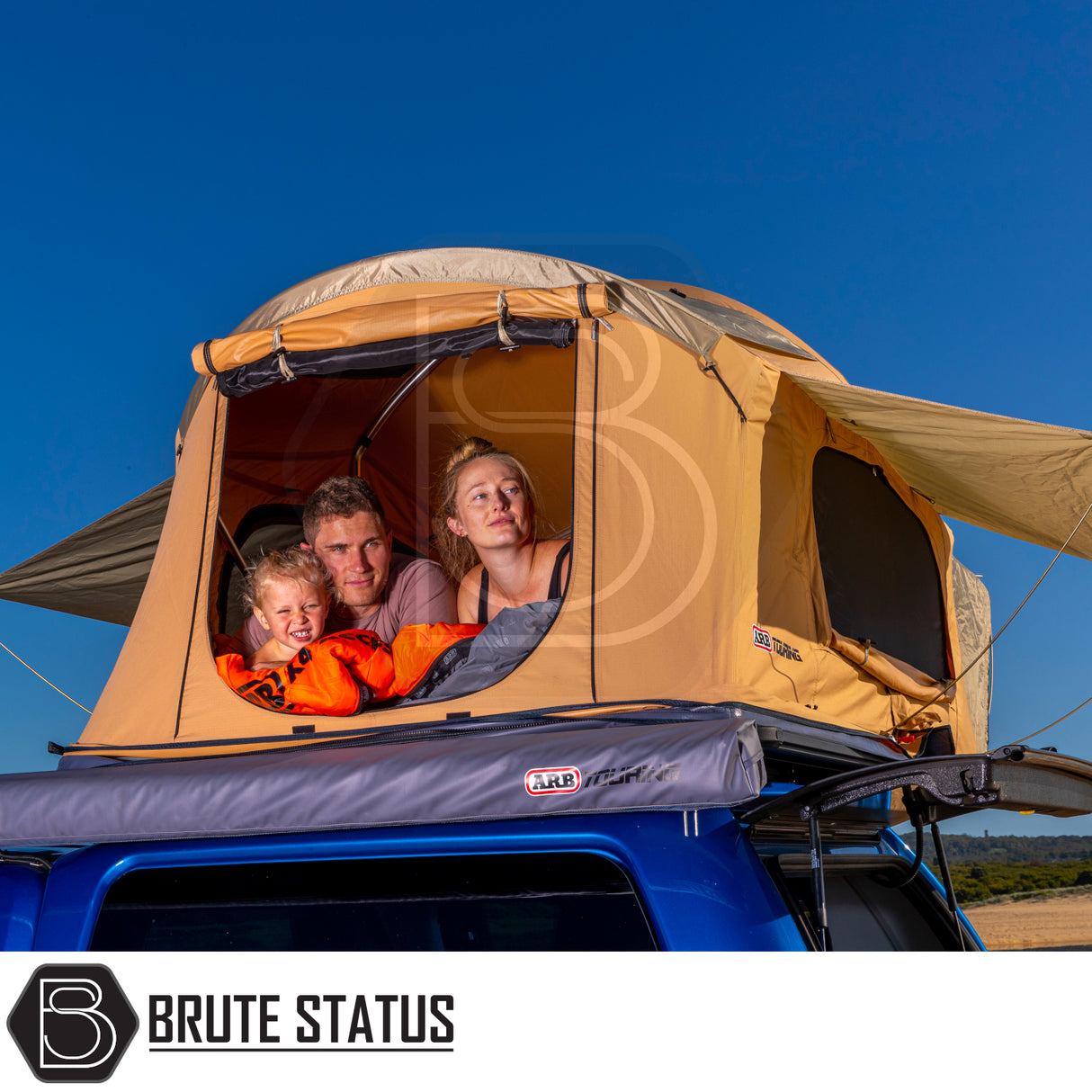 Blue vehicle with ARB Flinders Rooftop Tent, featuring a spacious interior, peeking family, and Brute Status logo, capturing an adventurous camping scene.