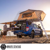 Blue pickup with ARB Flinders Rooftop Tent, awning, and slide-out kitchen on a beach, illustrating a compact, comfortable camping setup at sunrise.