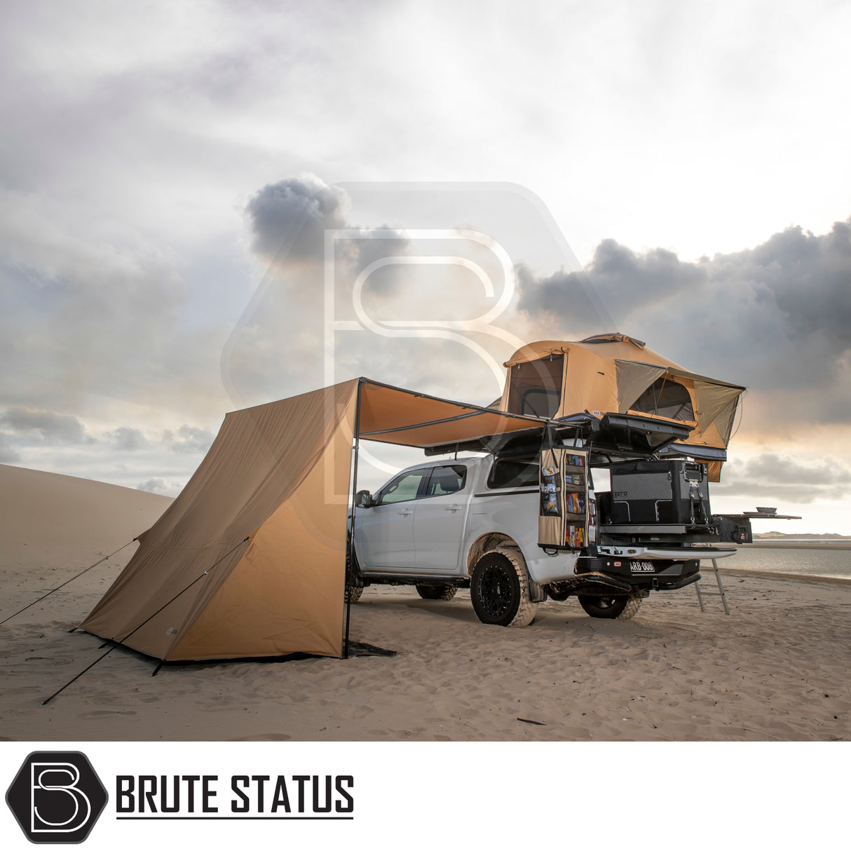 White 4x4 ute with ARB Flinders Rooftop Tent, awning, and pull-out kitchen on sandy beach, showcasing Brute Status camping gear setup.