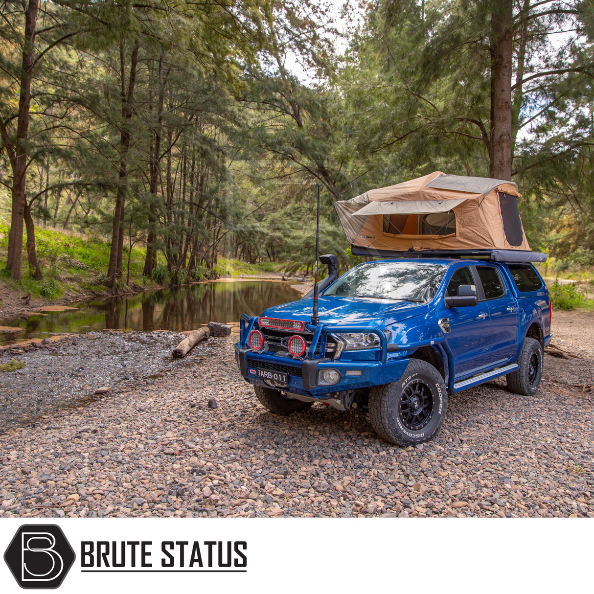 Blue 4x4 with ARB Flinders Rooftop Tent deployed, parked on rocky riverbank. Tent enhances comfort and utility for adventurous camping.
