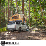 Pickup truck with ARB Flinders Rooftop Tent, featuring a fold-out design and aluminum ladder, parked in a forest clearing under tall trees.