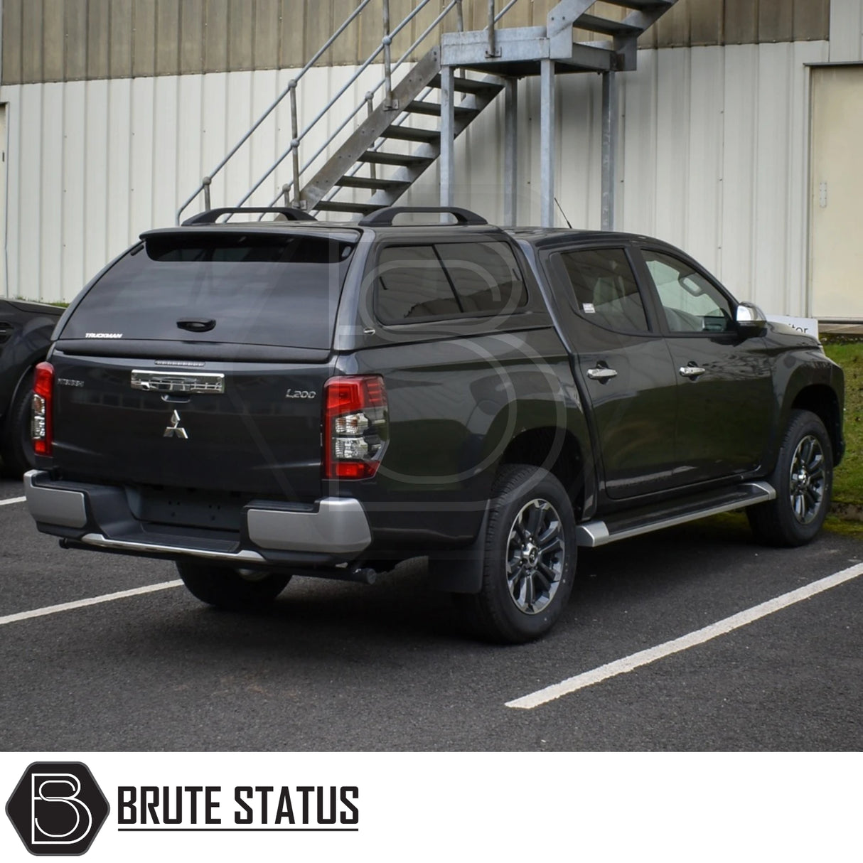 Mitsubishi L200 with Truckman GLS hardtop canopy featuring remote locking, tinted windows, and roof rails, parked near an industrial building.