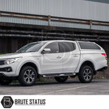 White double-cab pickup with a Truckman Grand hardtop canopy, remote locking, and alloy wheels, parked before an industrial wall, embodying Brute Status's custom truck enhancements.