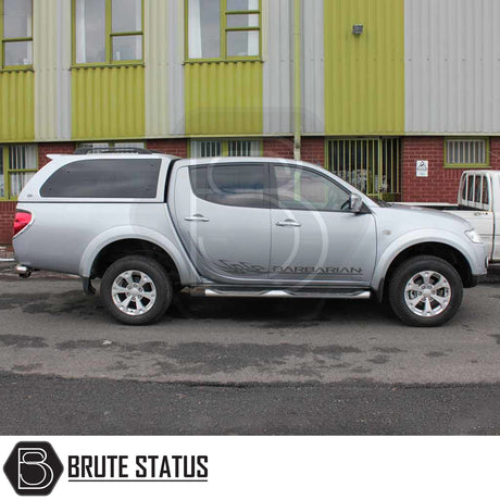 Silver Mitsubishi L200 Series 4 pickup with Truckman Grand Hardtop Canopy parked by industrial building, showcasing remote locking and tinted windows.