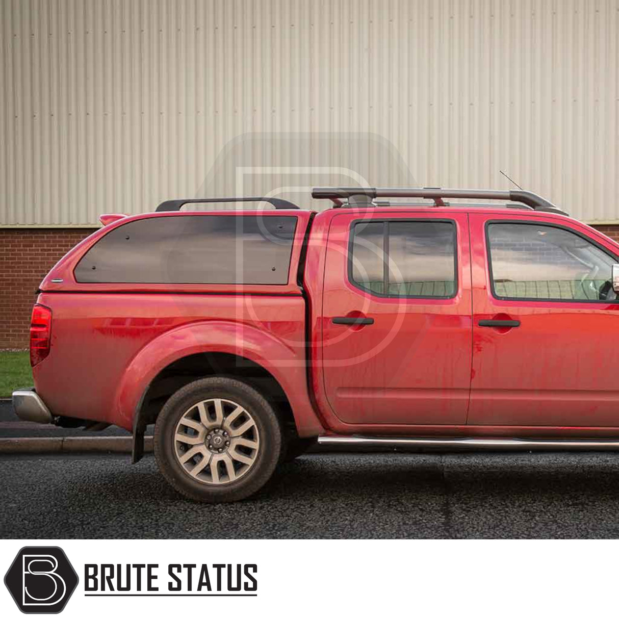 Side view of a Nissan Navara 2005-2015 D40 with Truckman Grand Hardtop Canopy, featuring tinted windows and roof-rack crossbars, parked in front of a building.