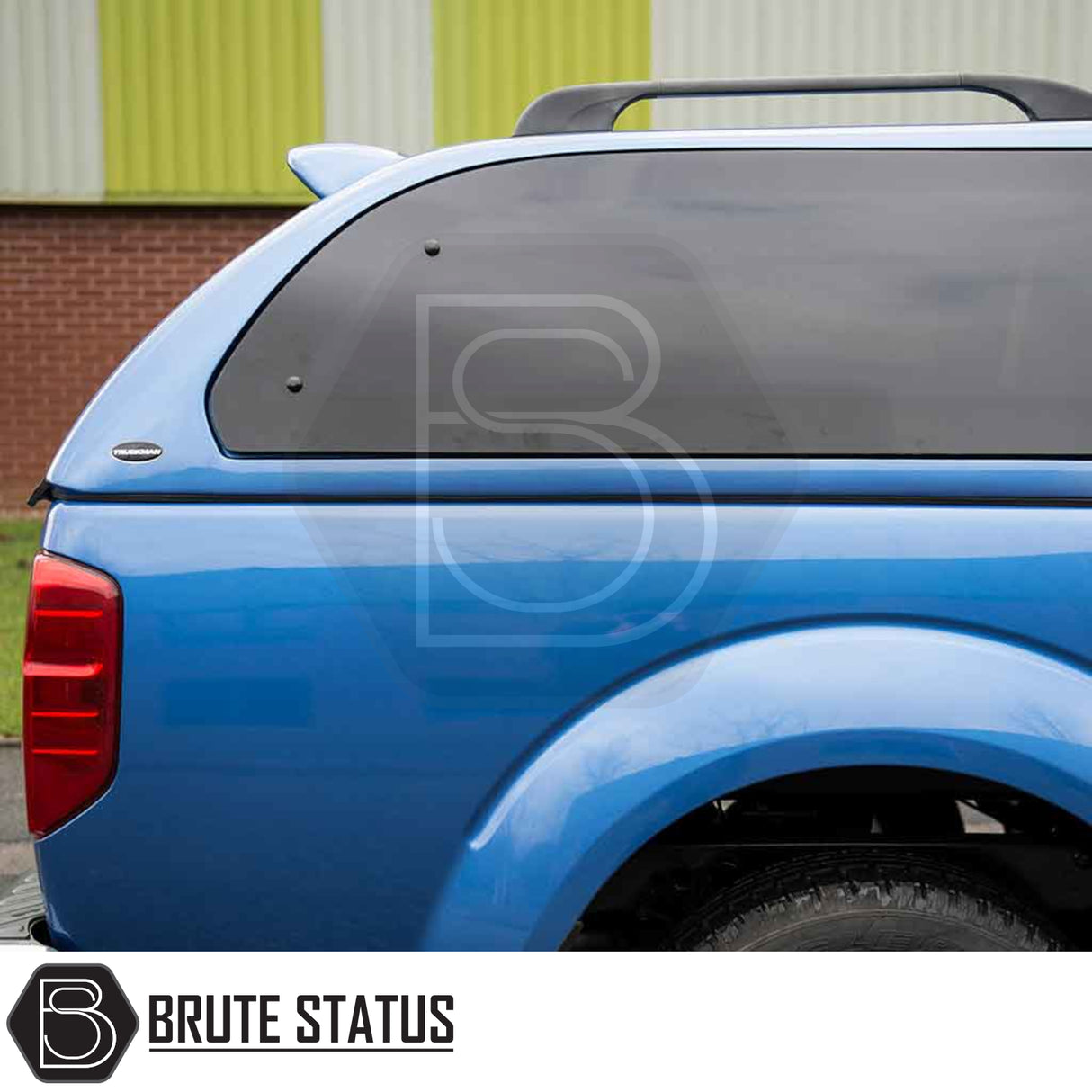 Rear view of a blue Nissan Navara 2005-2015 D40 with a Truckman Grand Hardtop Canopy featuring tinted windows and roof rails, branded by Brute Status.